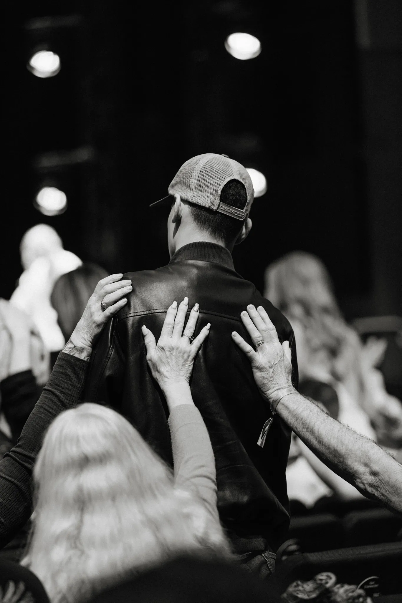A woman raises her hands toward the stage in a blue-lit worshipping crowd.
