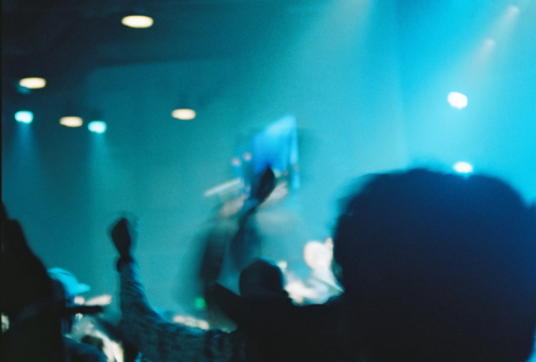 A film photo of a young man on stage smiling with arms raised, holding a microphone.
