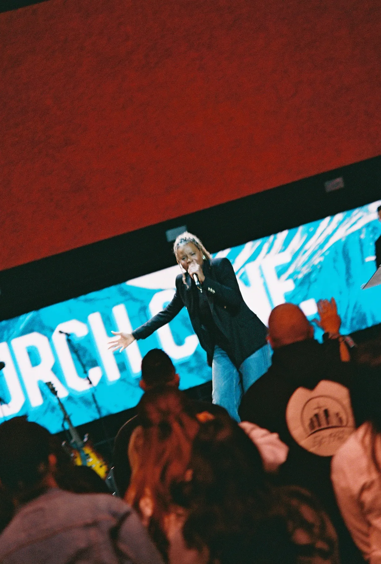 A film photo of a woman singing on stage in front of a teal backdrop reading part of "Church Conference."